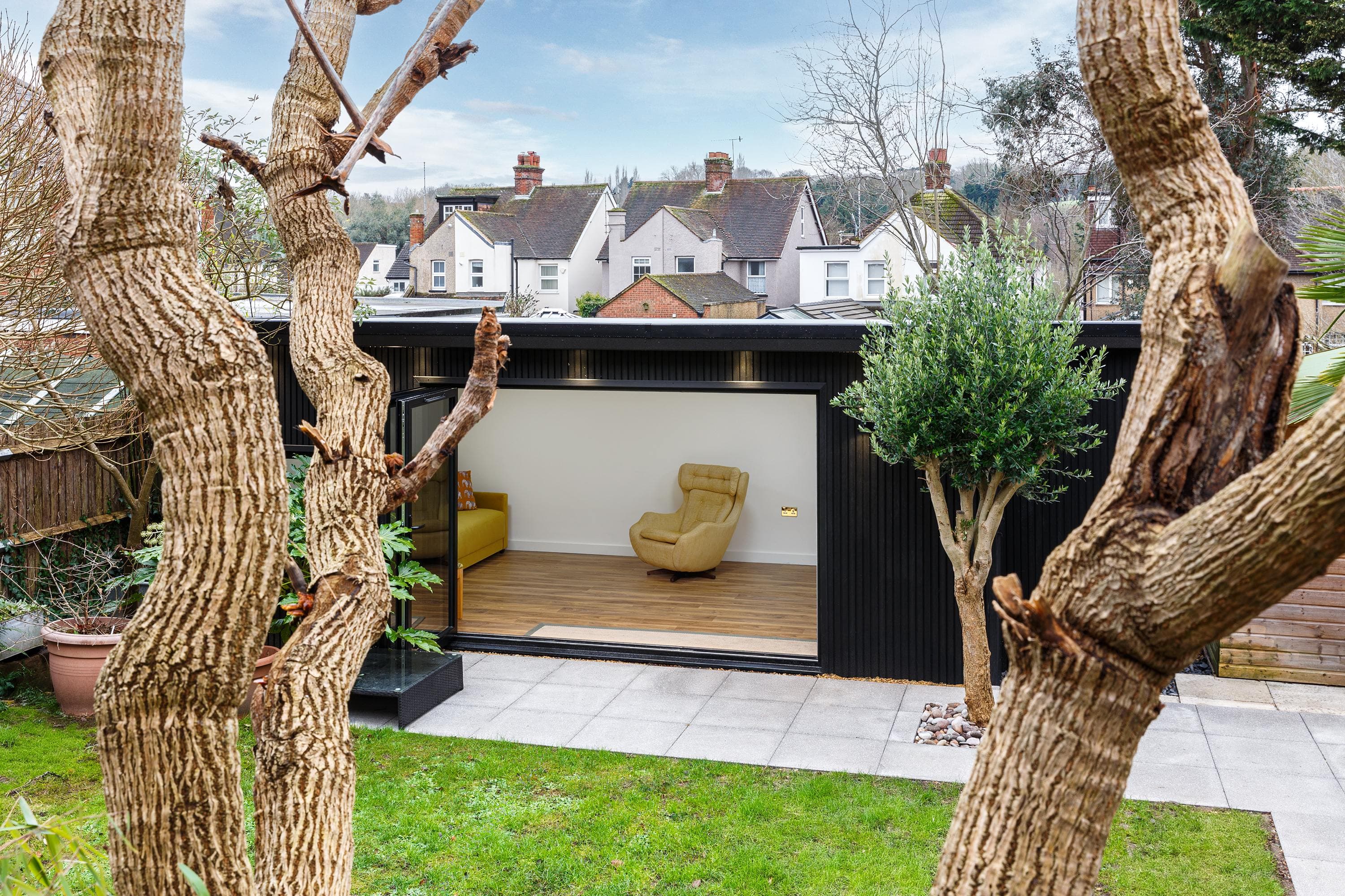 Black-clad garden studio in Bedfordshire with open sliding doors revealing a yellow armchair, seen across a lawn