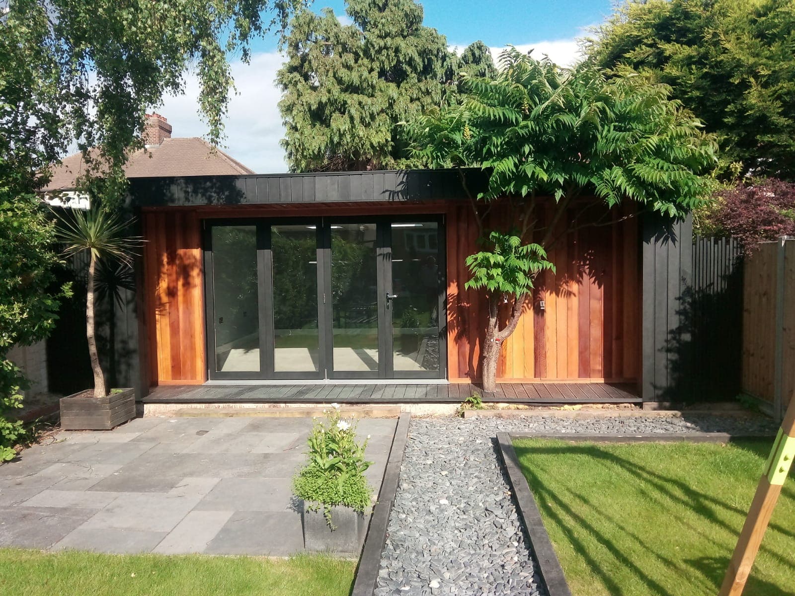 Cedar and black-clad garden room in Bedfordshire with grey bifold doors and a slate patio approach