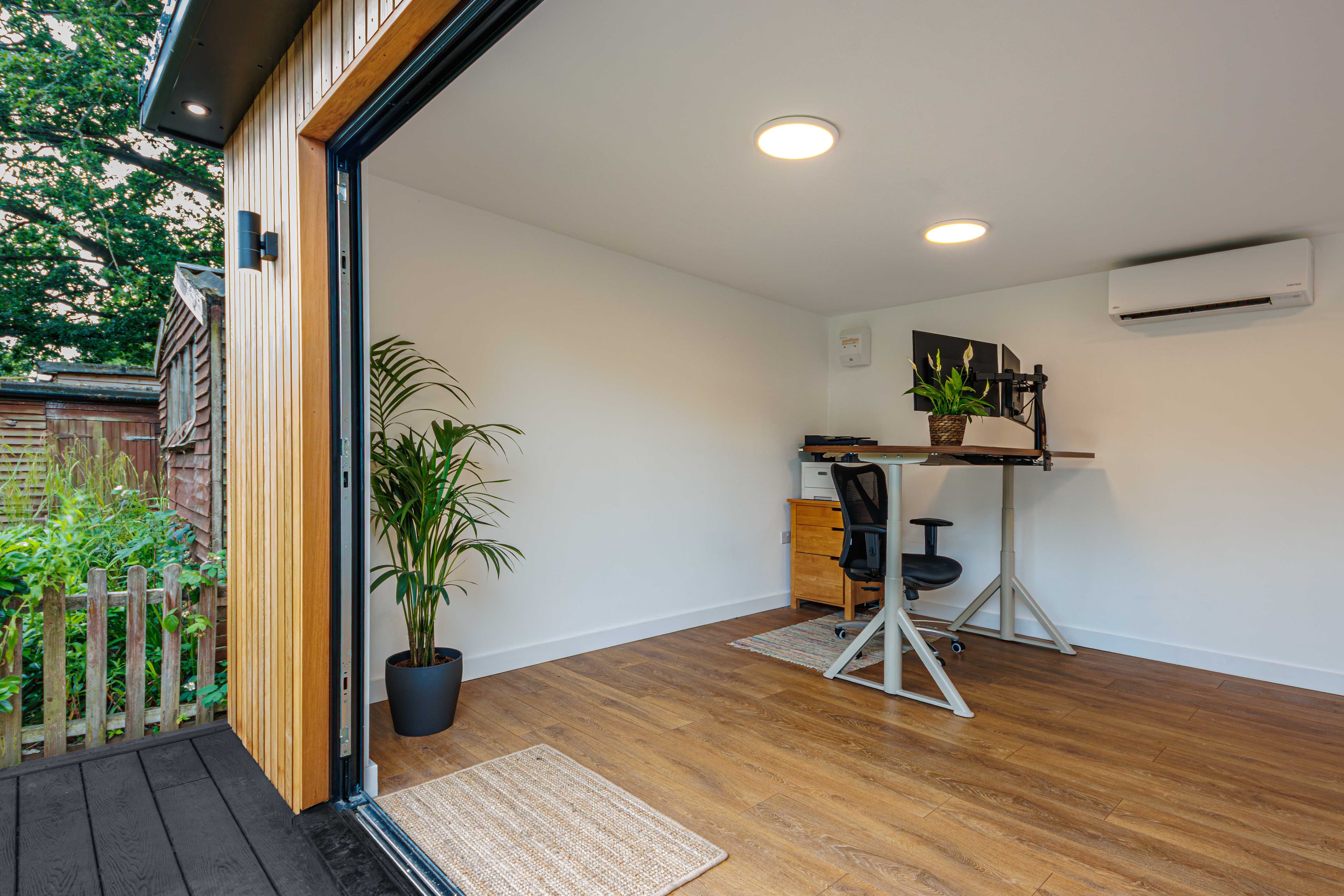 Garden office interior in Bedfordshire with a standing desk, air conditioning unit and bifold doors to the garden