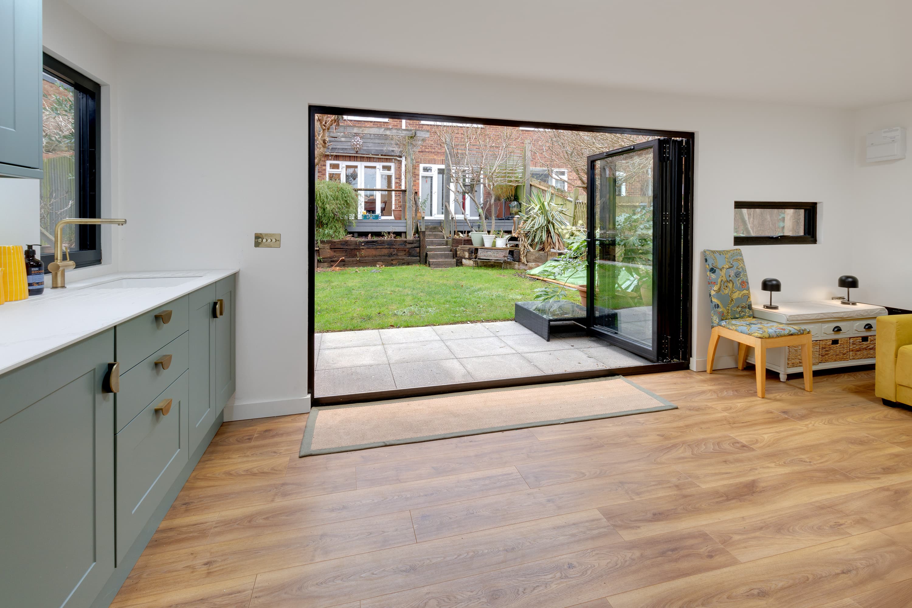 Garden room interior in Bedfordshire with sage-green kitchen units and wood flooring, black bifold doors open to the garden