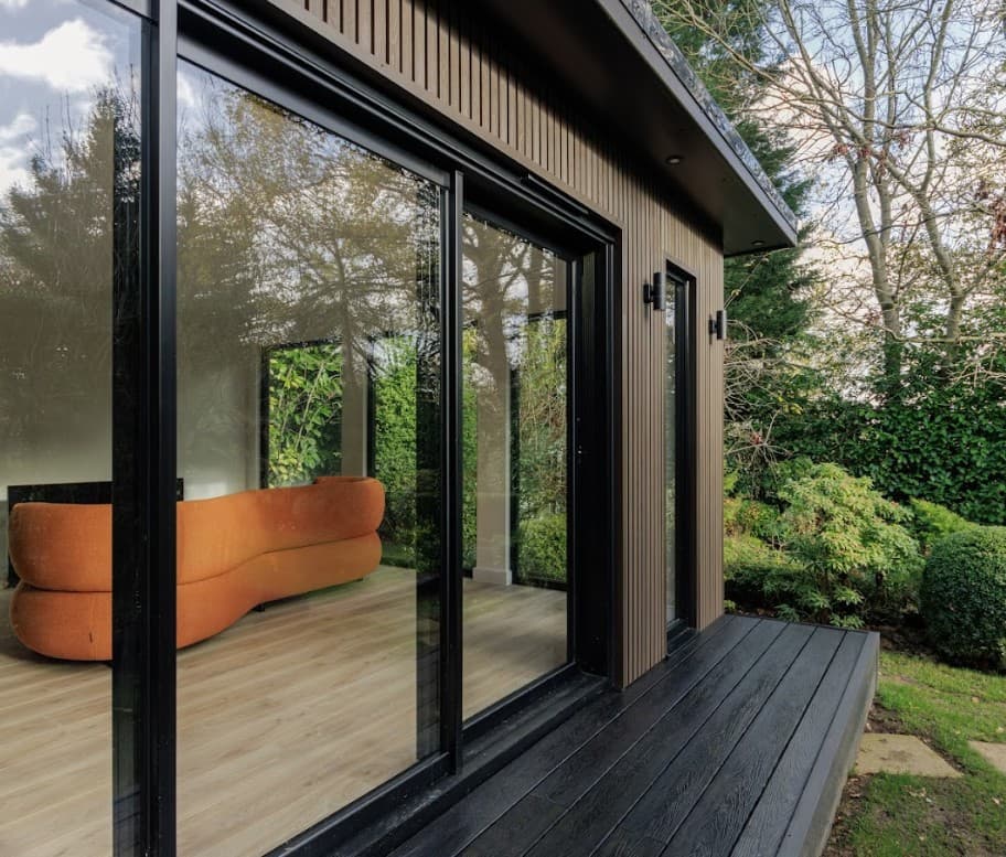 Walnut slatted-clad garden room in Bedfordshire with sliding doors and an orange sofa inside