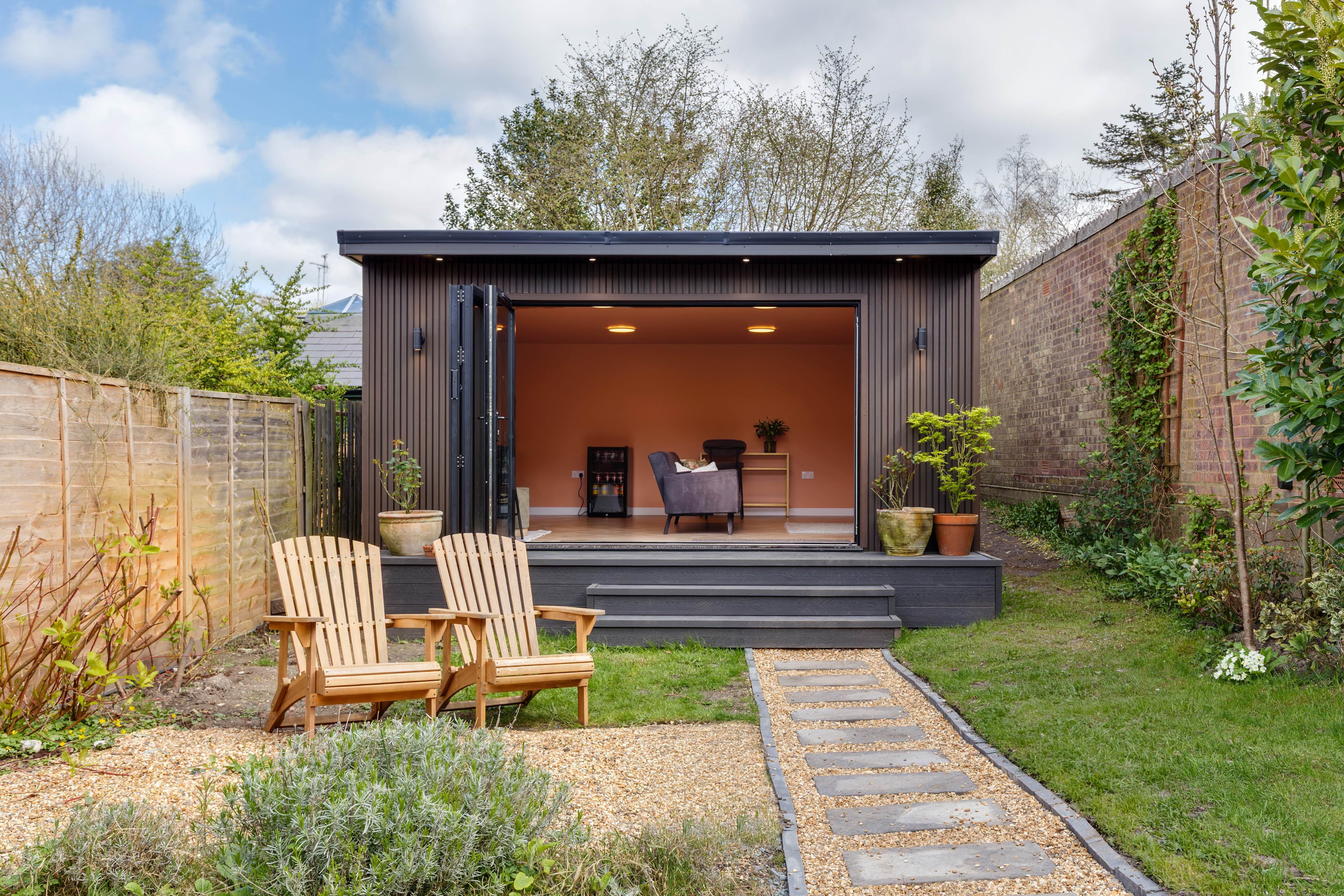 Charcoal garden room in Bedfordshire with bifold doors open onto a terracotta-painted lounge and Adirondack chairs on the lawn