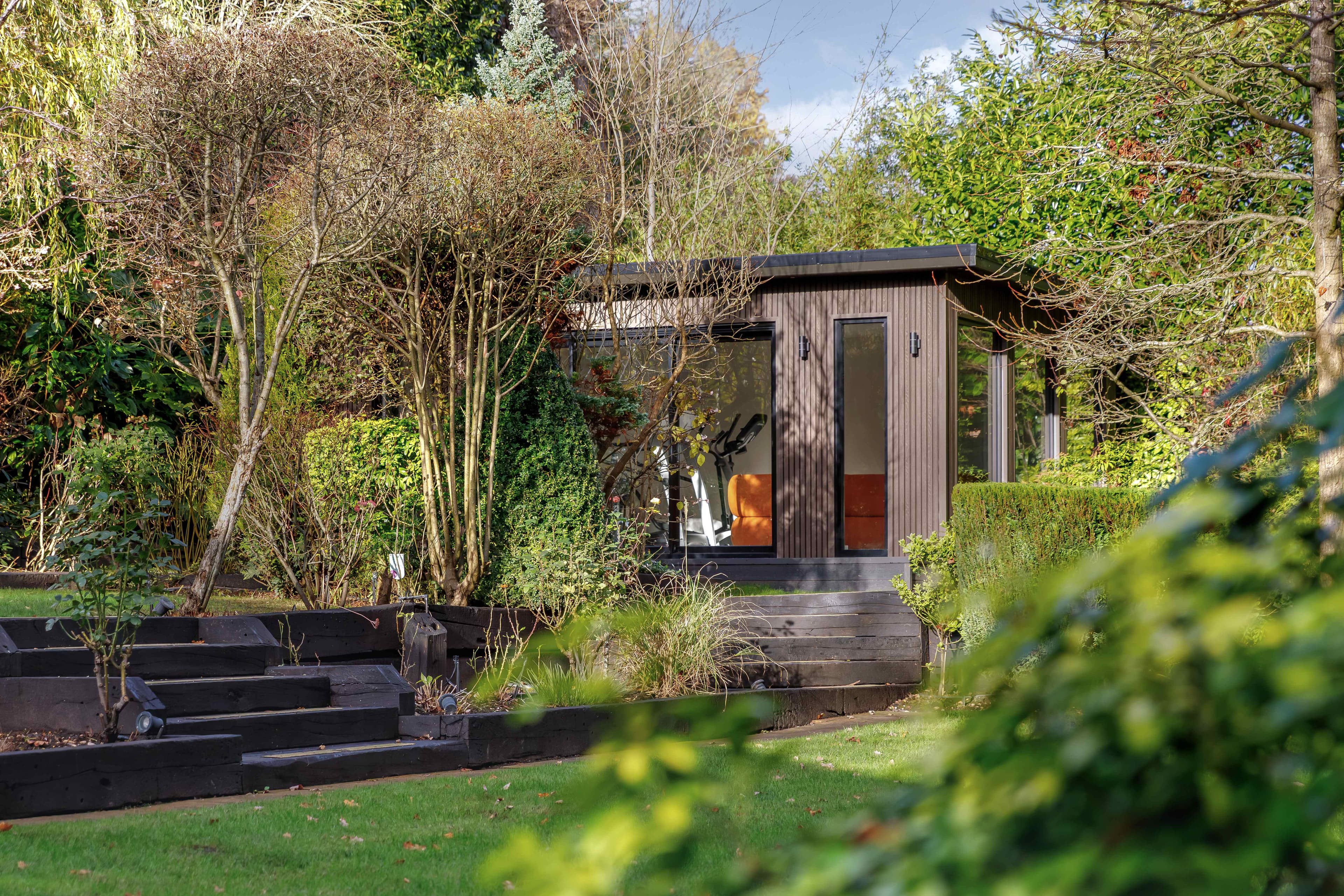 Dark timber-clad garden room in Bedfordshire set in a mature landscaped garden with railway-sleeper steps