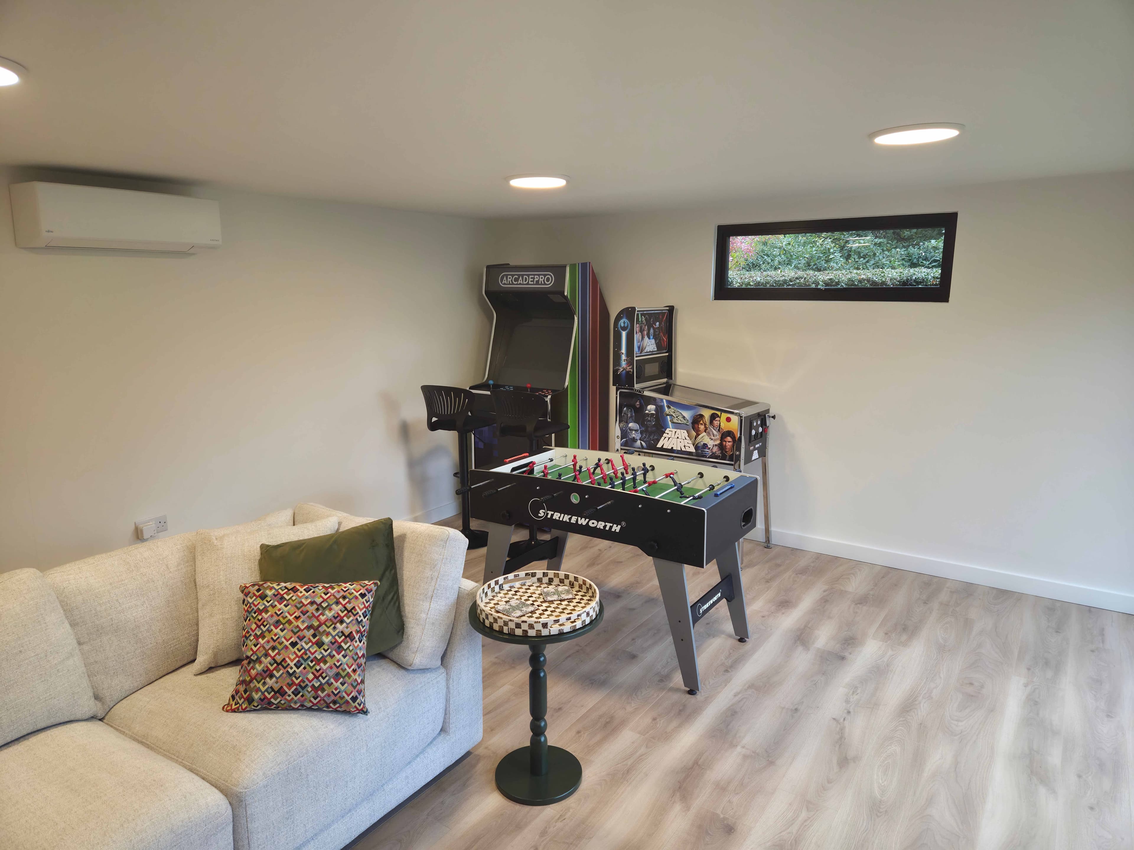 Garden room in Bedfordshire fitted out as a games room with an arcade machine, pinball, foosball table and sofa
