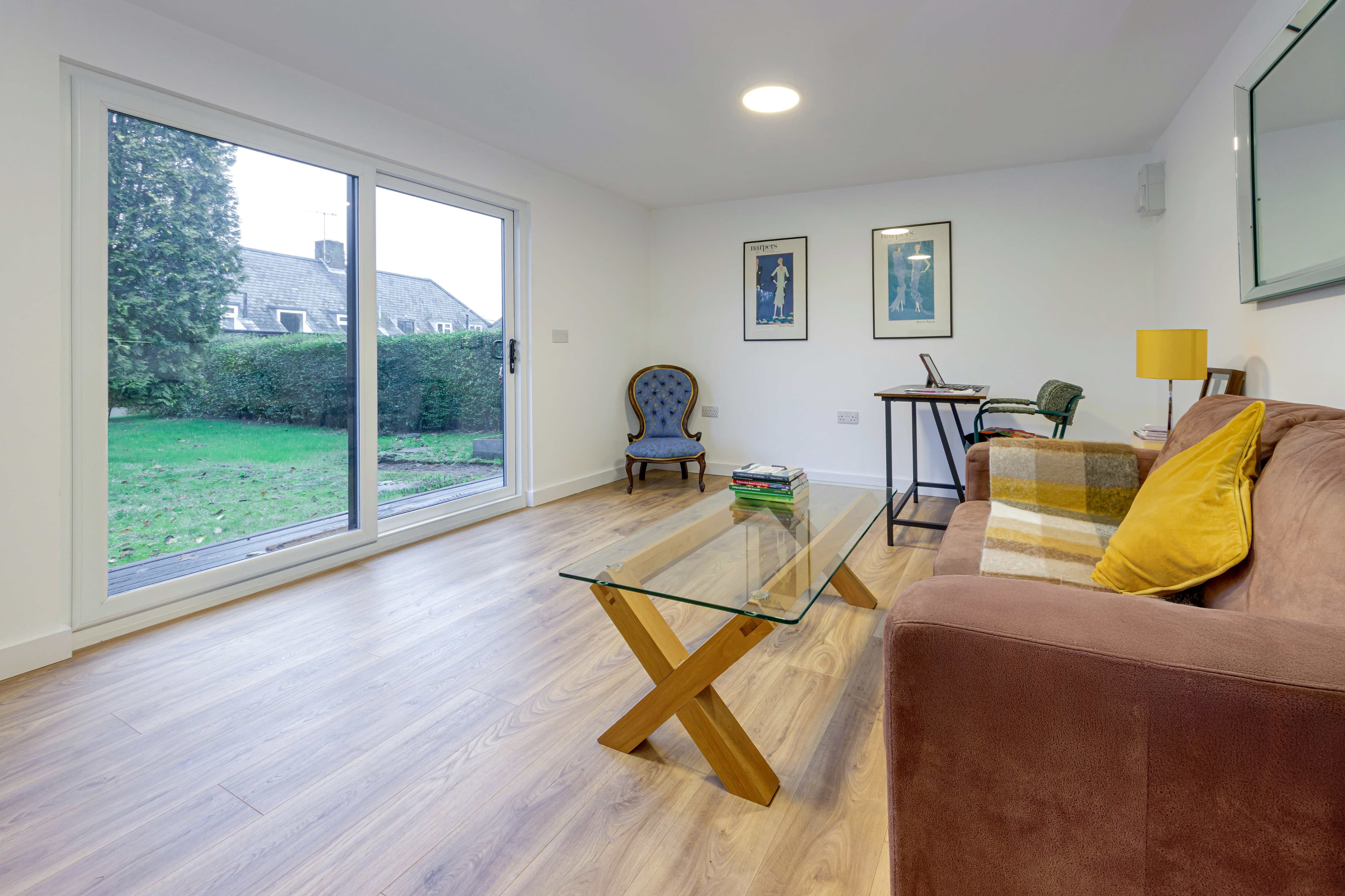 Bright garden room lounge in Bedfordshire with a brown sofa, glass coffee table and full-height sliding doors onto the garden