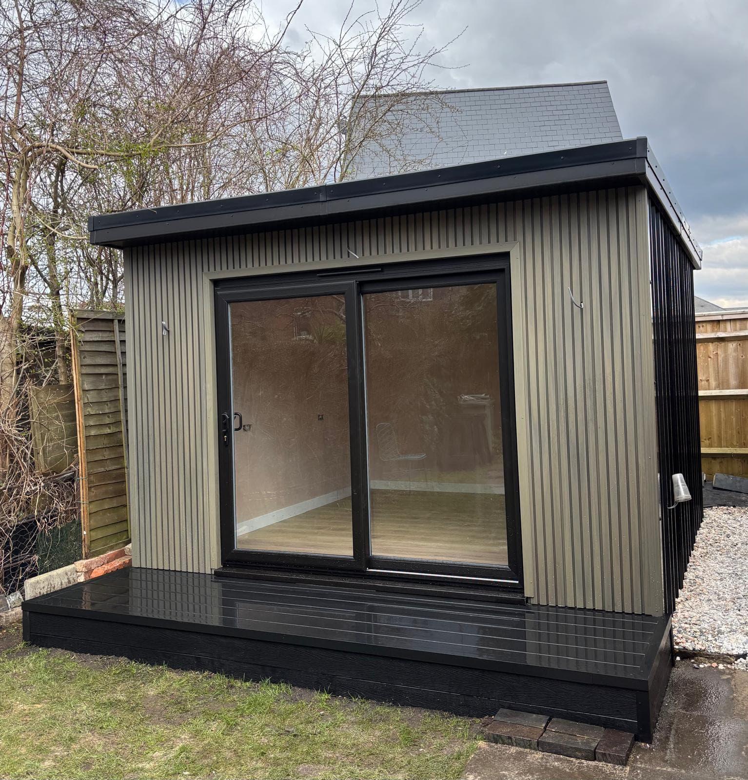 Insulated garden room in Bedfordshire with greige corrugated cladding, a black composite deck and sliding glass doors