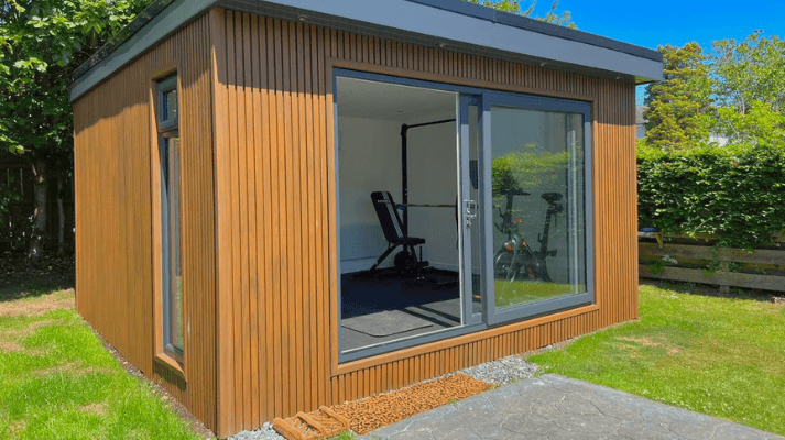Cedar slatted-clad garden gym in Bedfordshire with large sliding doors open to a weights bench and exercise bike on a sunny lawn