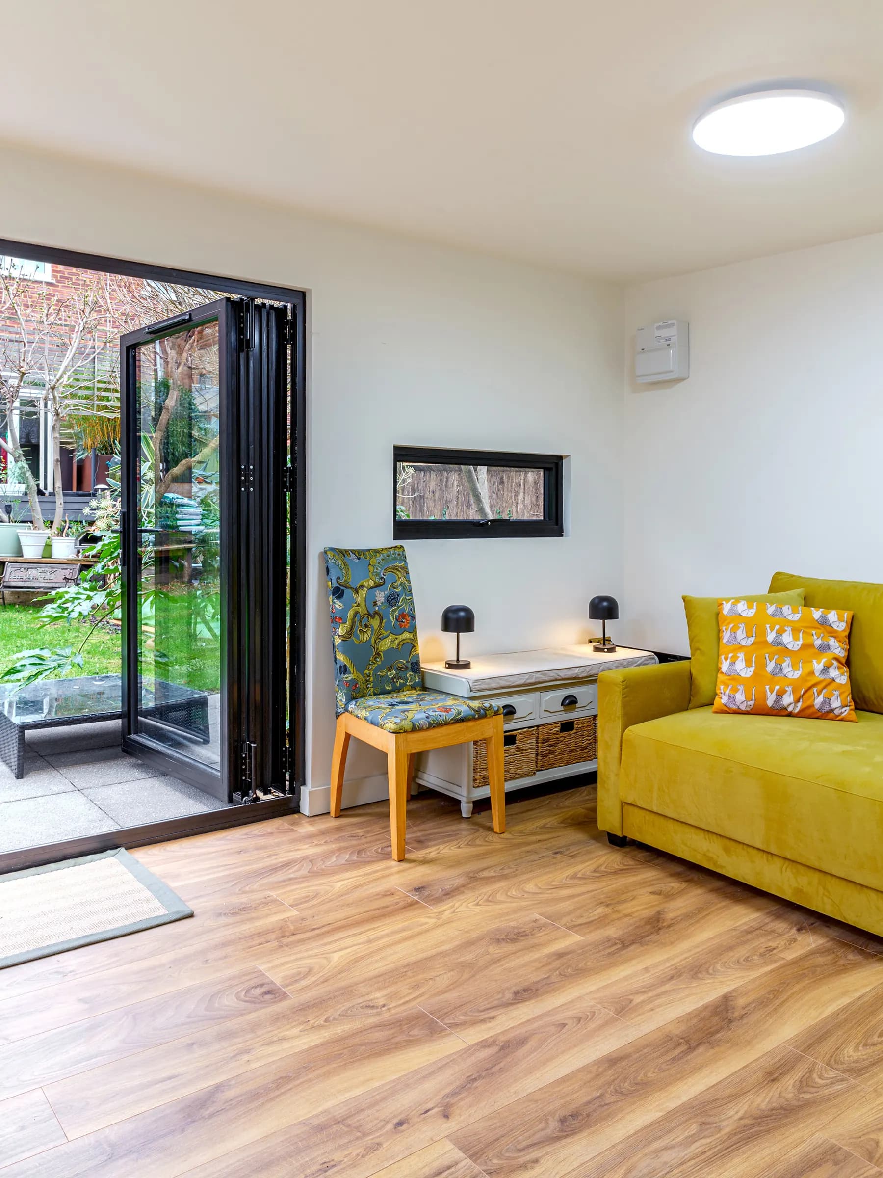 Garden annexe interior with yellow sofa, small desk and open glazed doors
