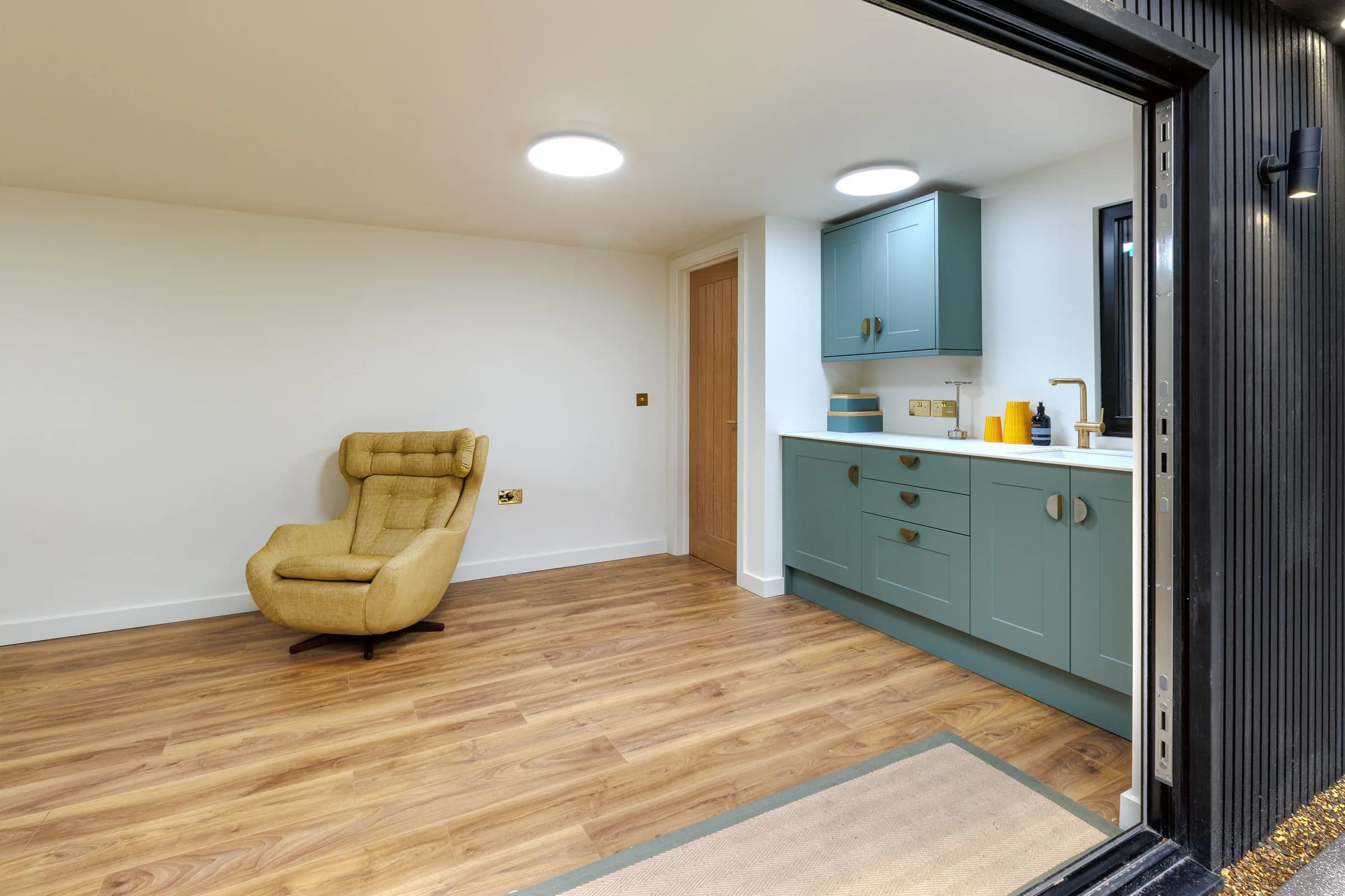 Garden annexe interior with green kitchenette, armchair and open glazed doors