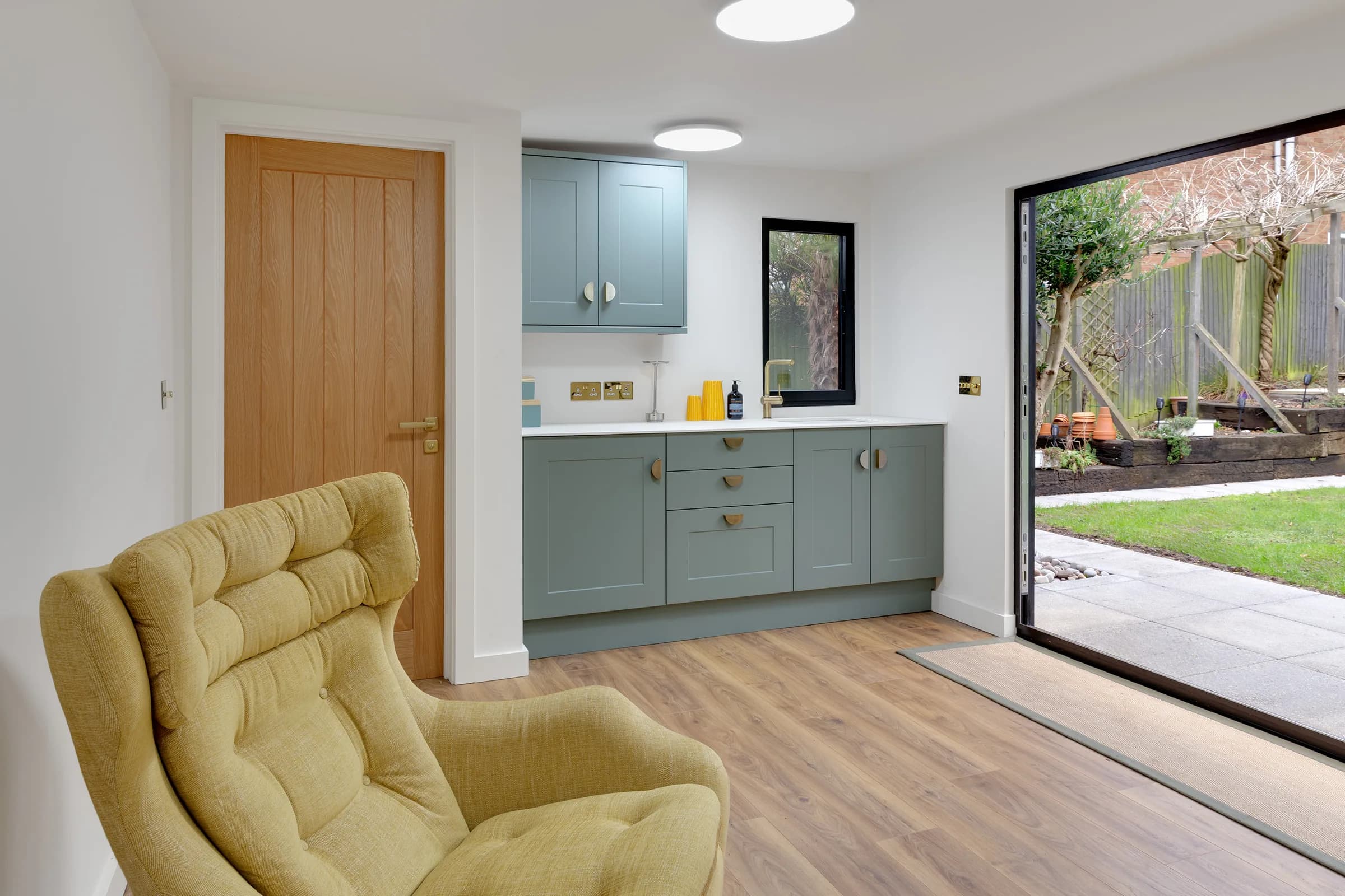 Garden annexe interior with green kitchenette, armchair and garden-facing glazed doors