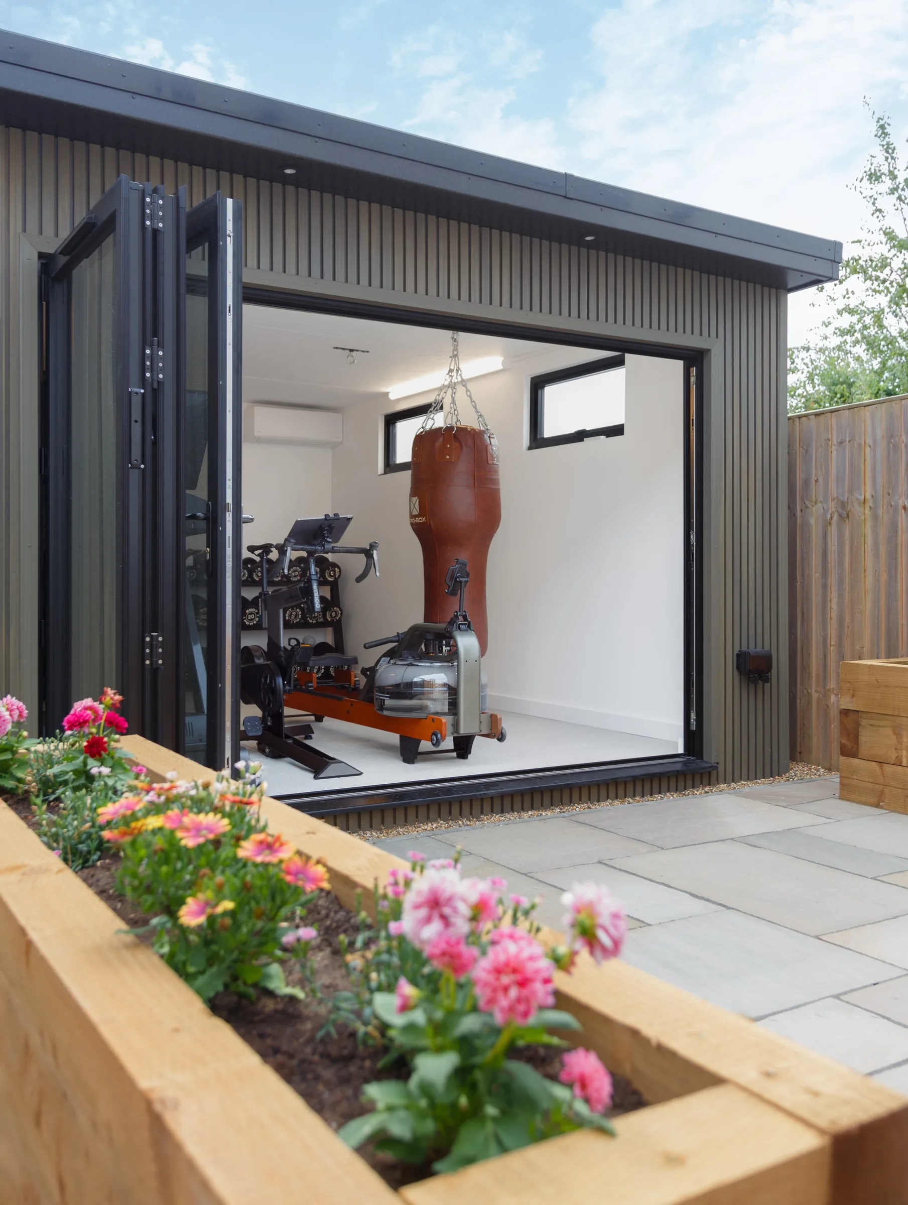 Garden gym with open doors and a punch bag, seen beyond a raised flower bed