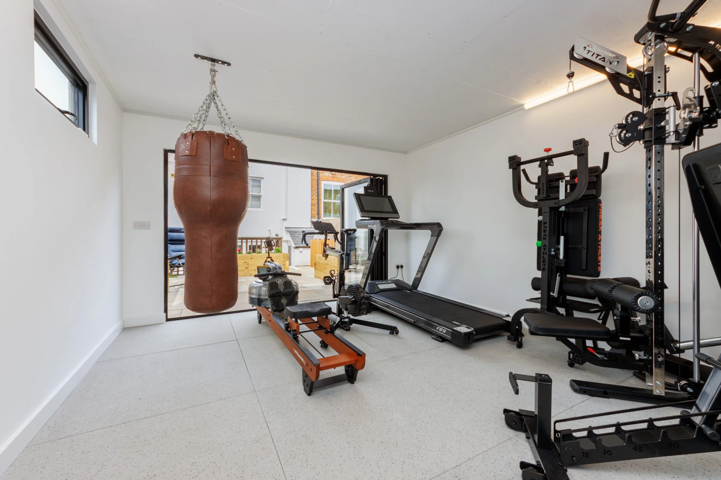 Garden gym interior with a punch bag, rowing machine, treadmill and weight station