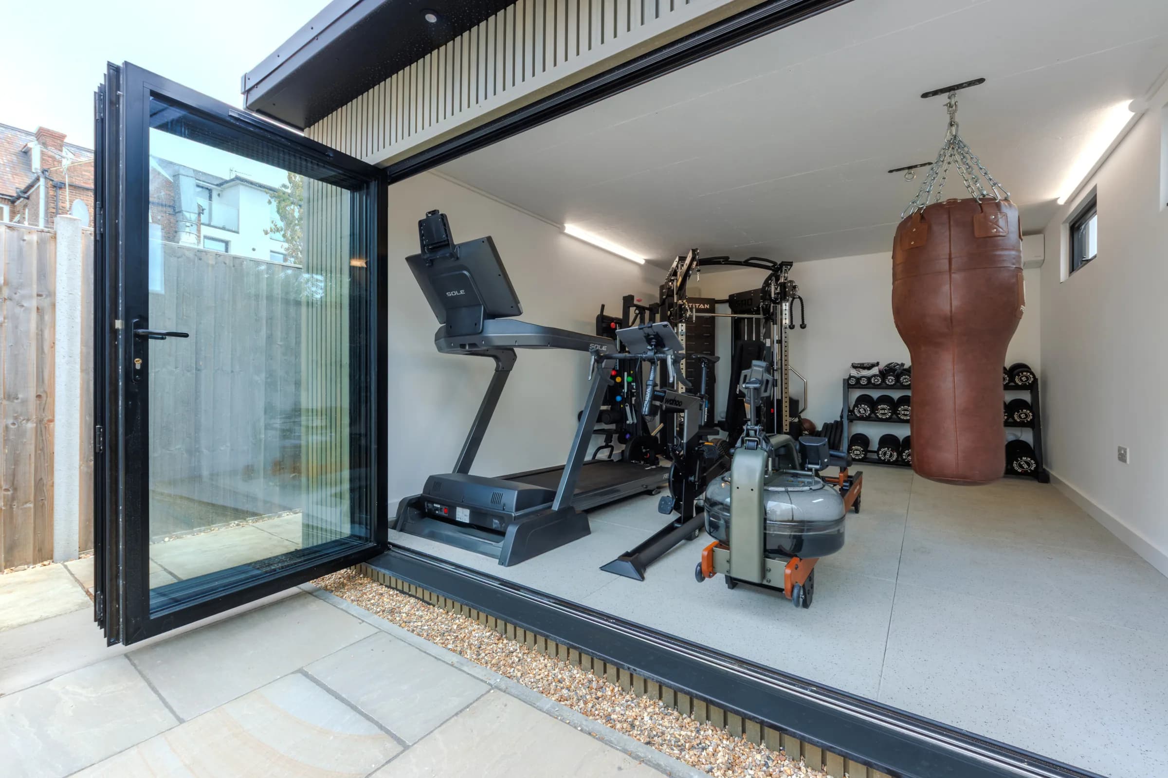 View through open garden gym doors towards a treadmill, weights and punch bag