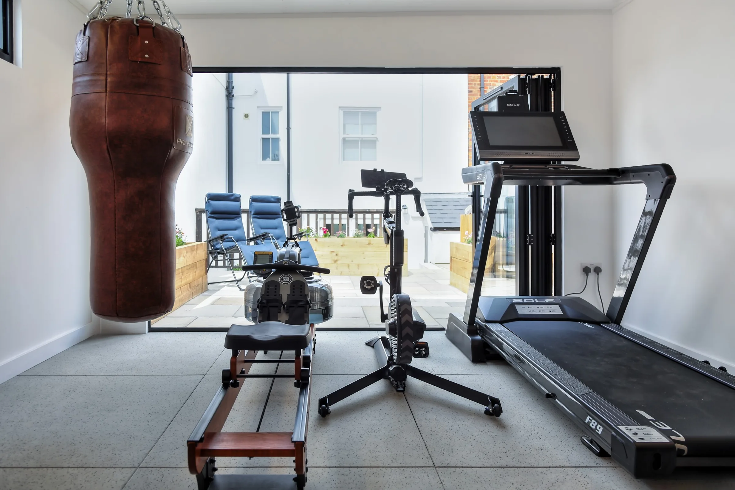 Garden gym interior facing the open doors, with punch bag, rowing machine and treadmill