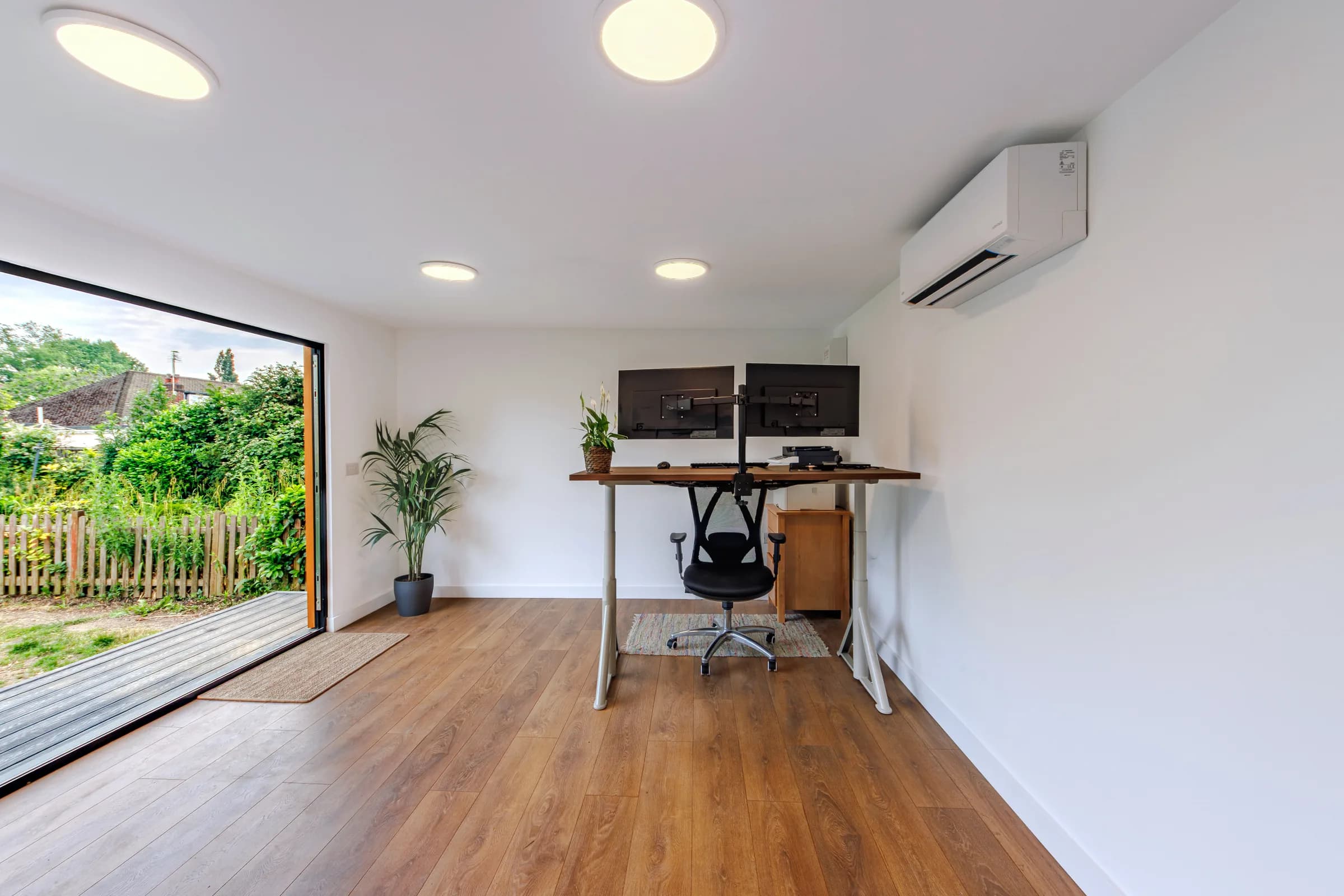Bright garden office interior with a standing desk, dual monitors and wall-mounted air conditioning