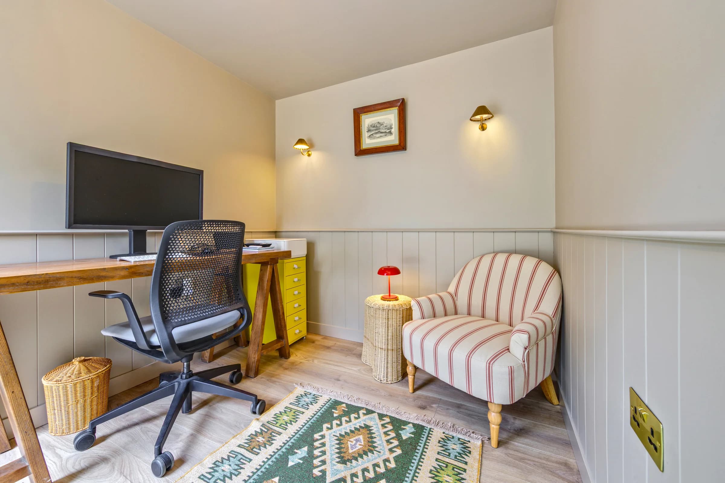 Garden office interior with a long desk, screen and striped armchair