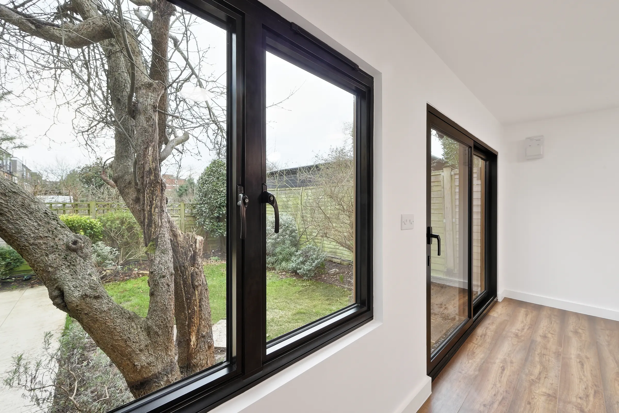 Close interior view of black-framed windows and a glazed door overlooking a tree