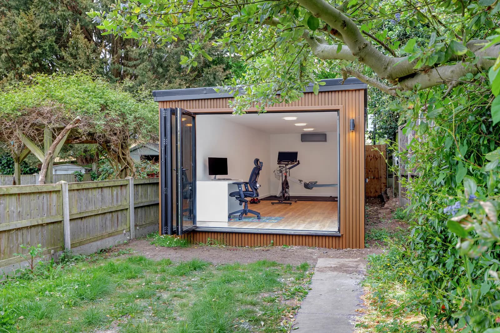 Timber-clad garden room with fully open doors and exercise equipment inside