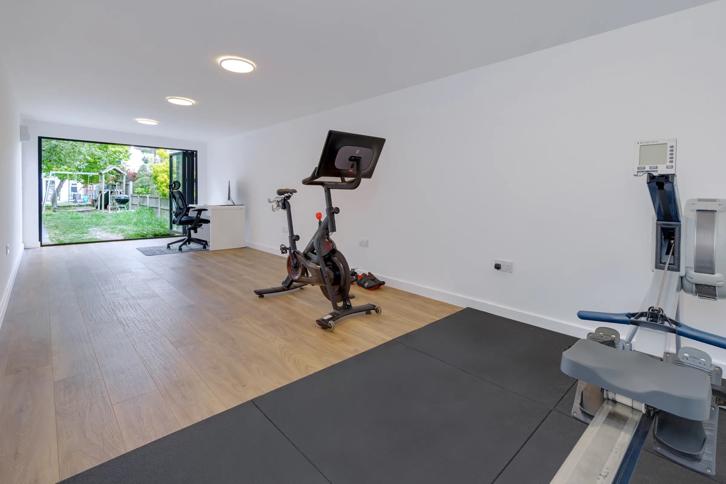 Garden room interior with exercise machines and a desk by open doors
