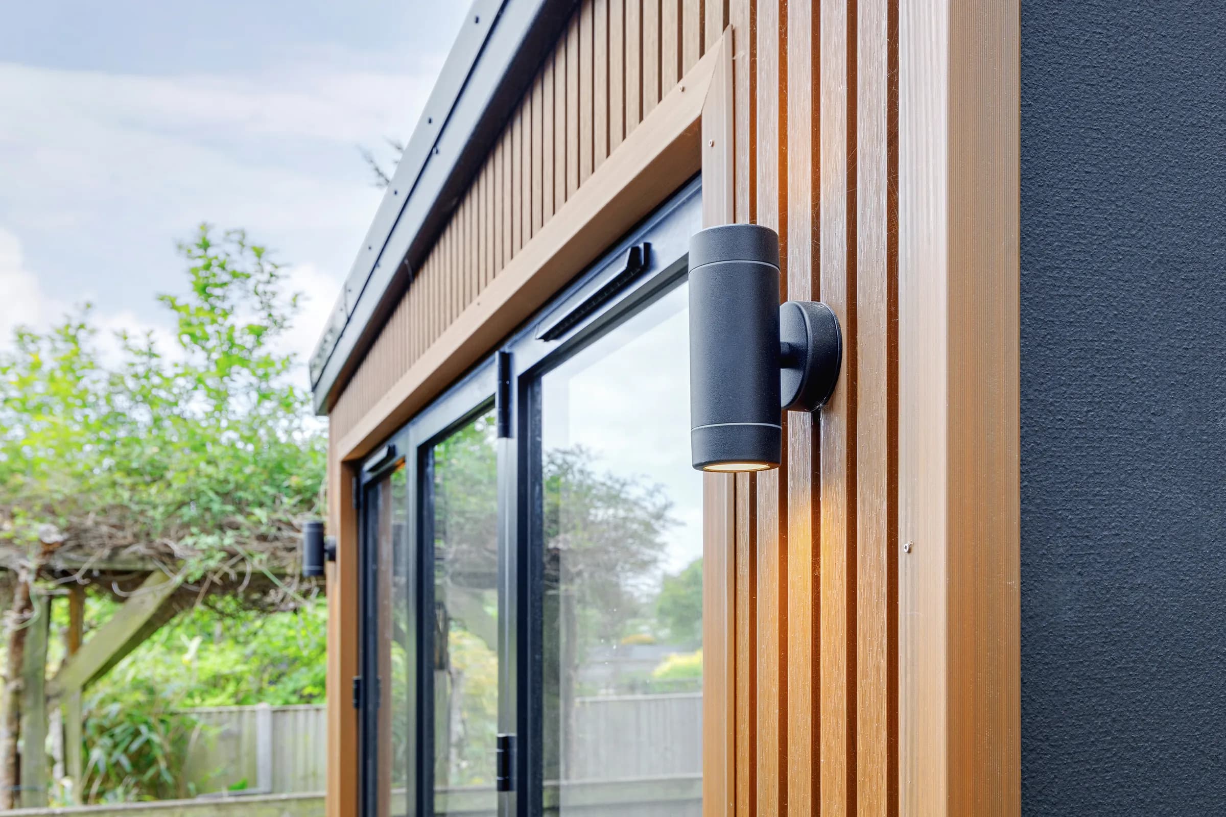 Close view of a garden room's vertical timber cladding, glazed doors and exterior light