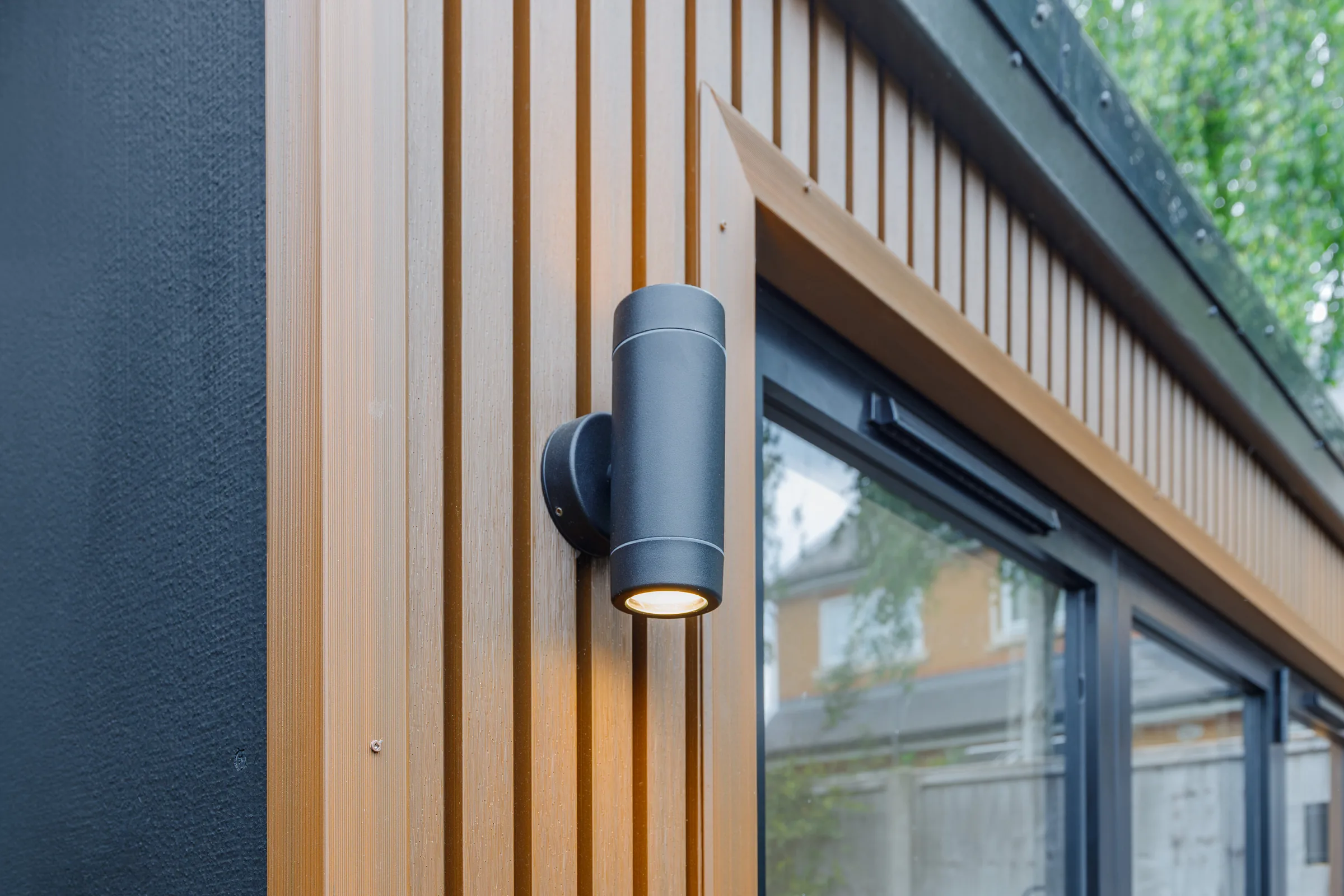Close view of vertical timber cladding and an exterior wall light beside glazing