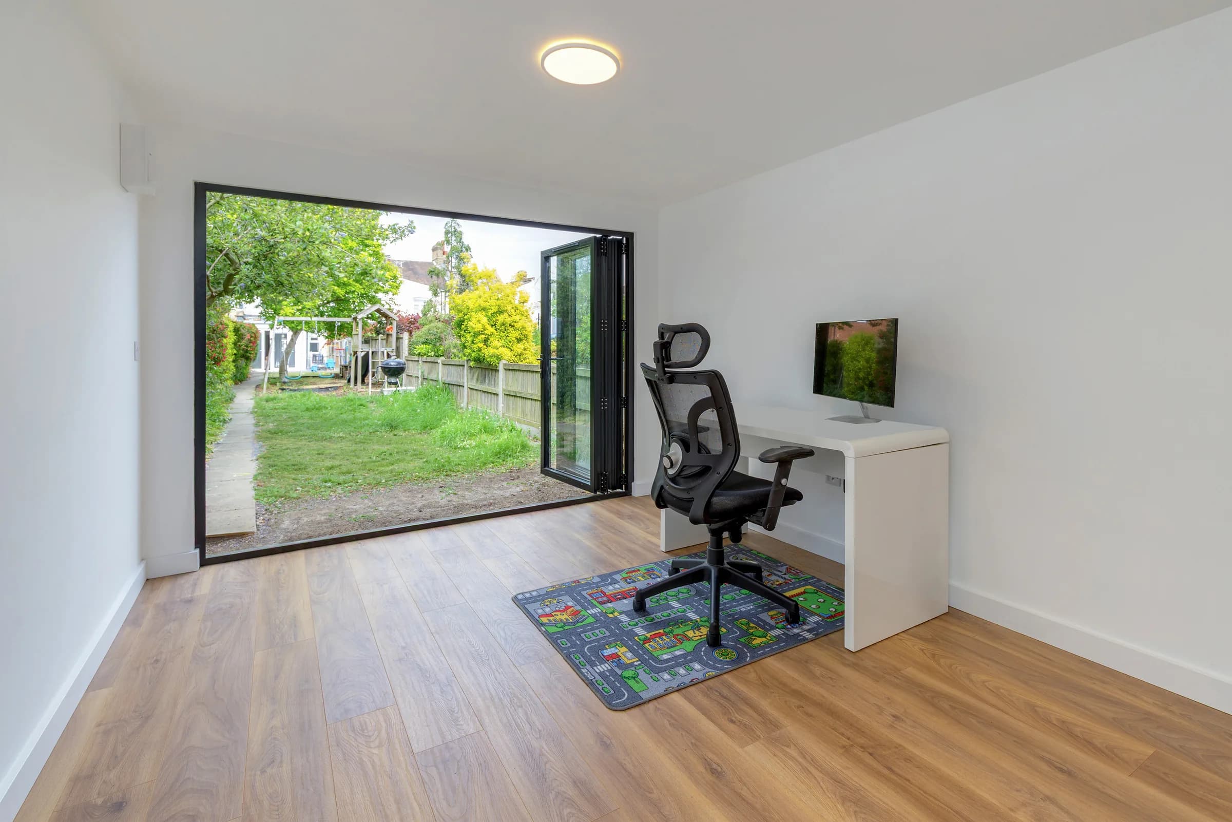 Garden room interior with a desk, office chair and exercise equipment by open doors
