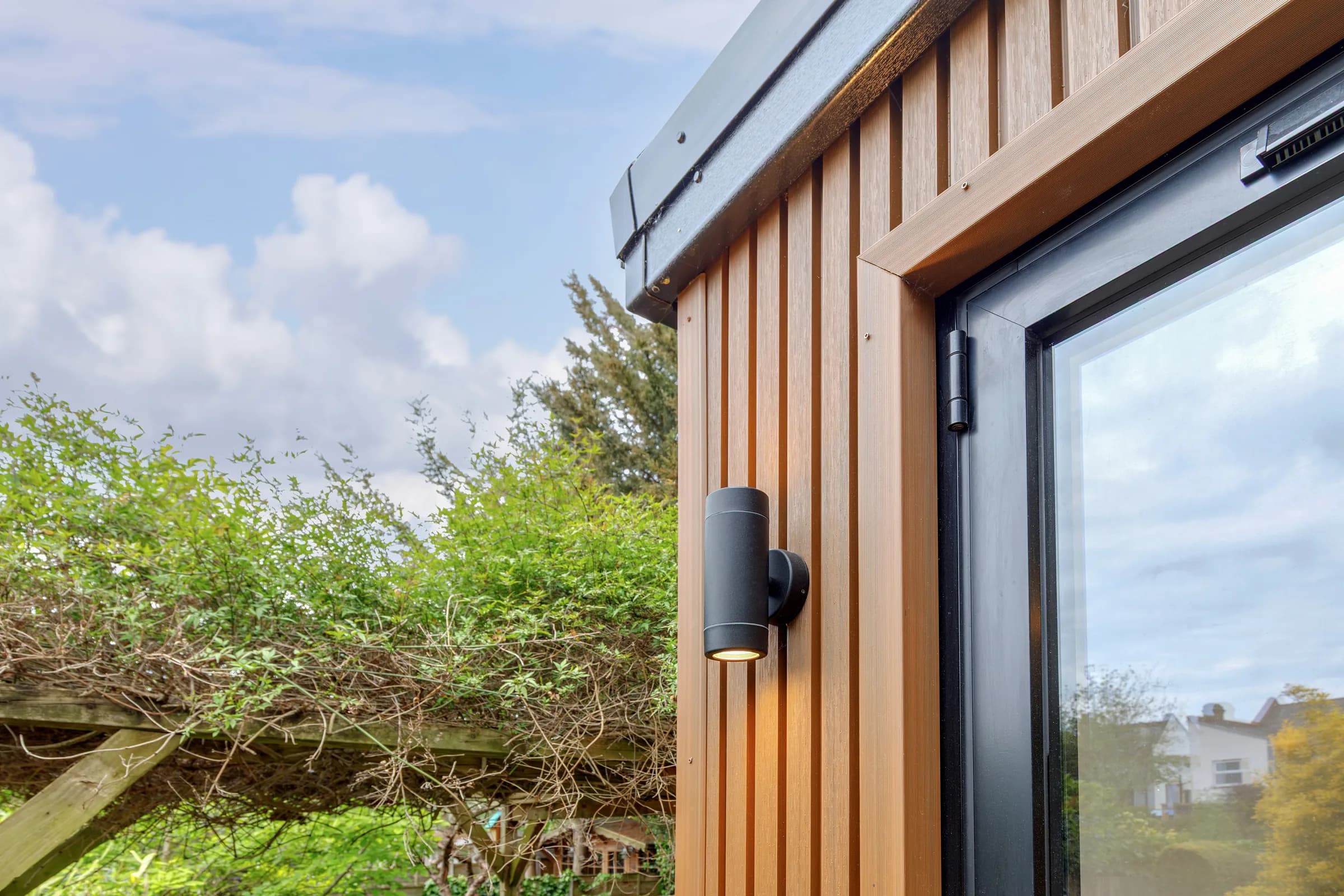 Upward view of timber cladding and an exterior light beside a glazed door