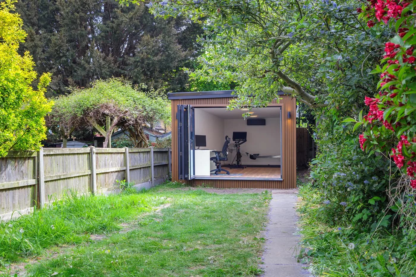 Garden room with fully open doors and exercise equipment, viewed along a garden path