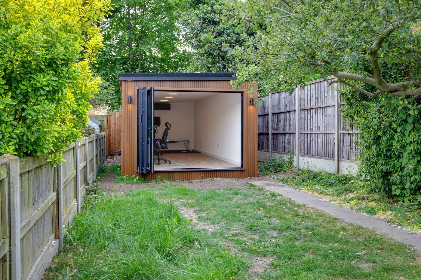 Timber-clad garden studio with fully open doors at the end of a lawn