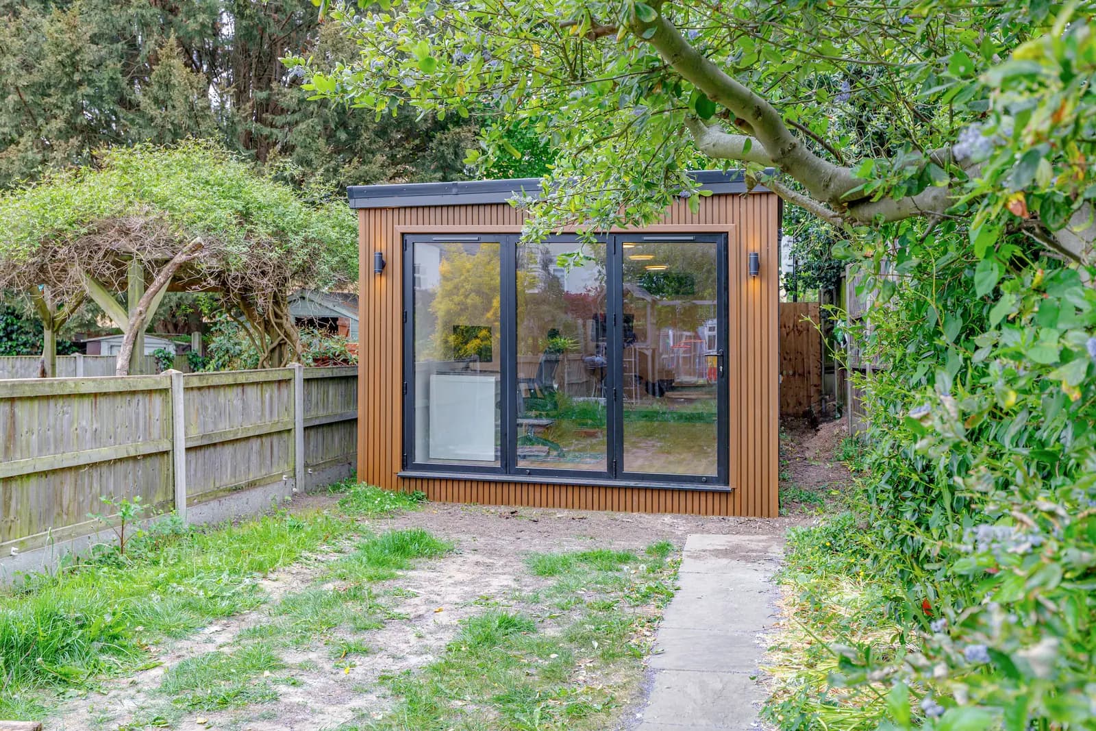 Timber-clad garden studio with closed glazed doors seen across the lawn