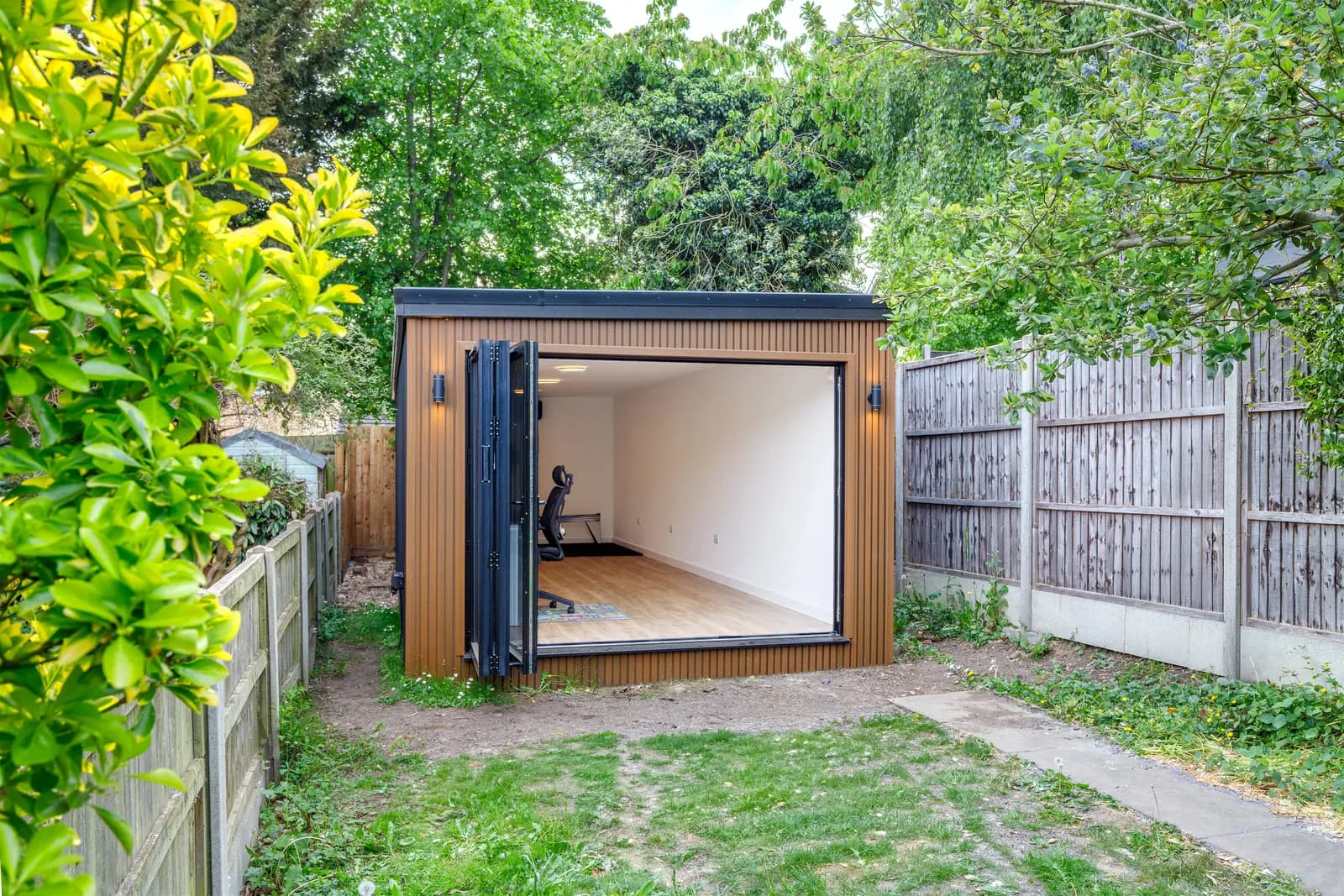 Garden studio with fully open doors, viewed between garden hedges
