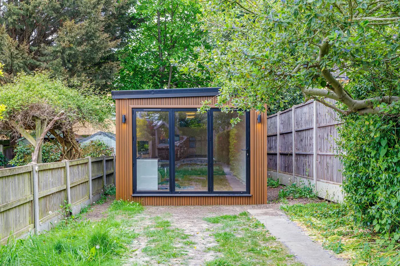 Timber-clad garden studio with closed glazed doors framed by leafy branches