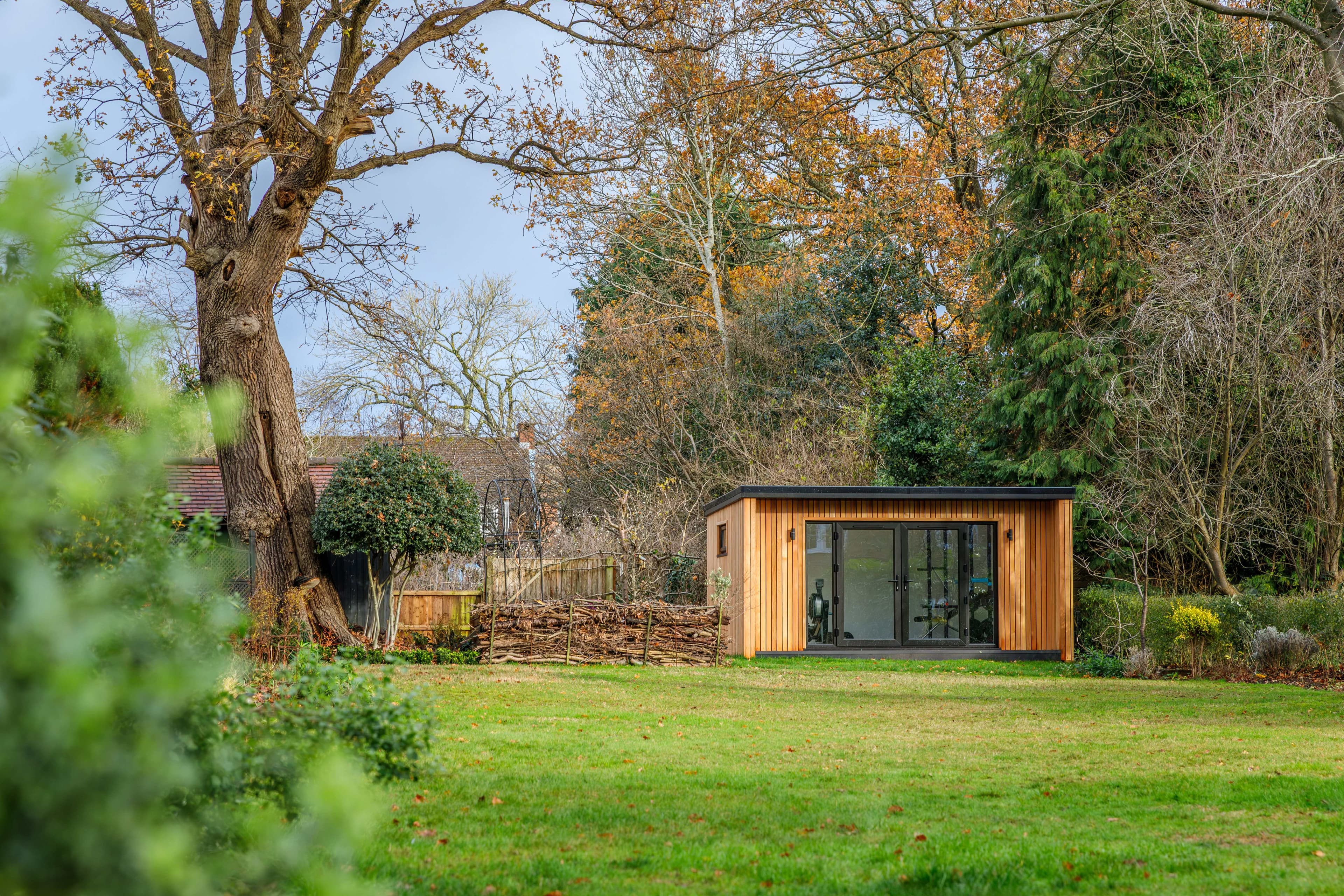 Cedar-clad garden room in the centre of a large Bedfordshire garden, framed by mature autumn trees