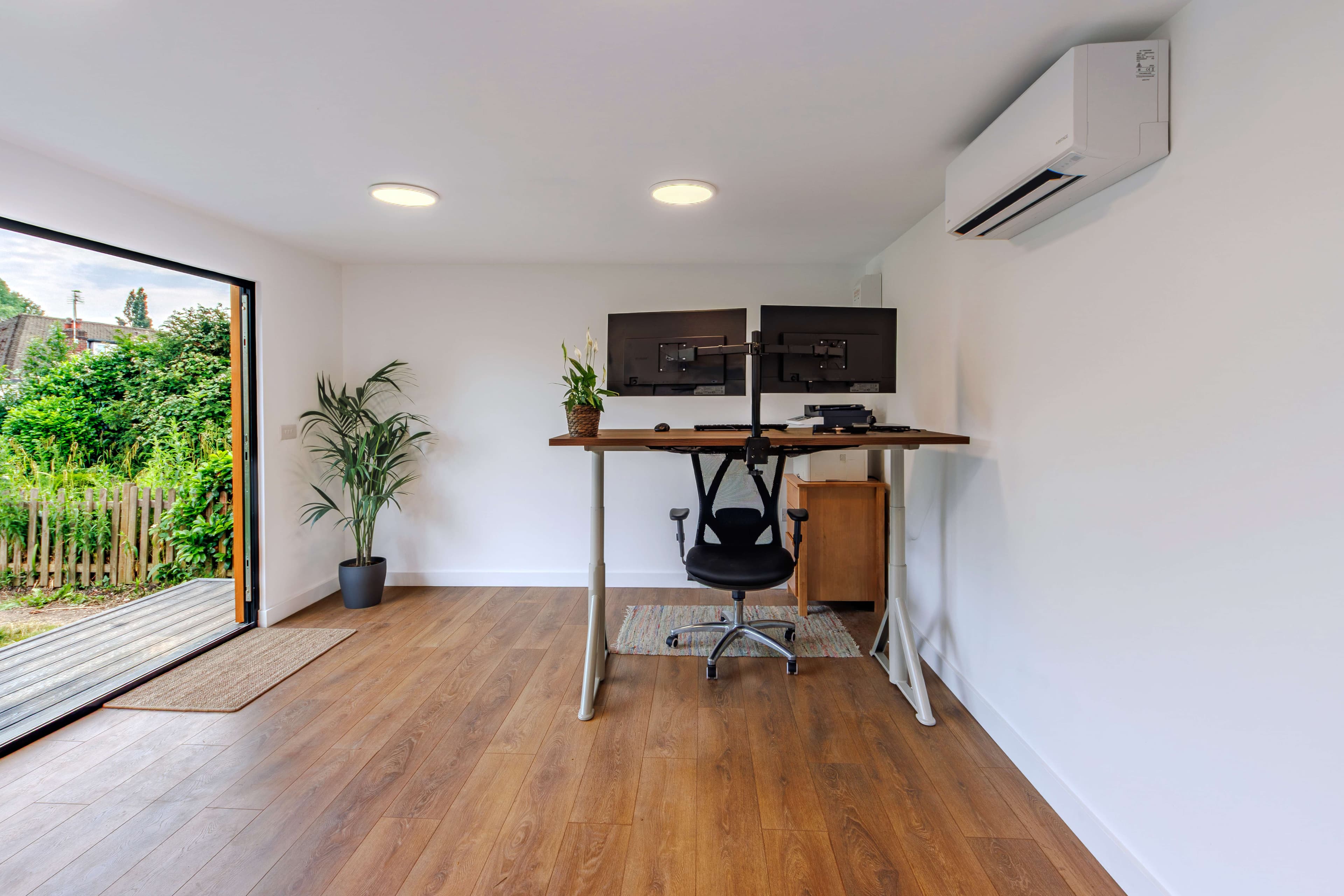 Garden office interior with a dual-monitor desk, air conditioning and bifold doors to the garden, of the kind Beds Garden Rooms builds for Bedfordshire homes