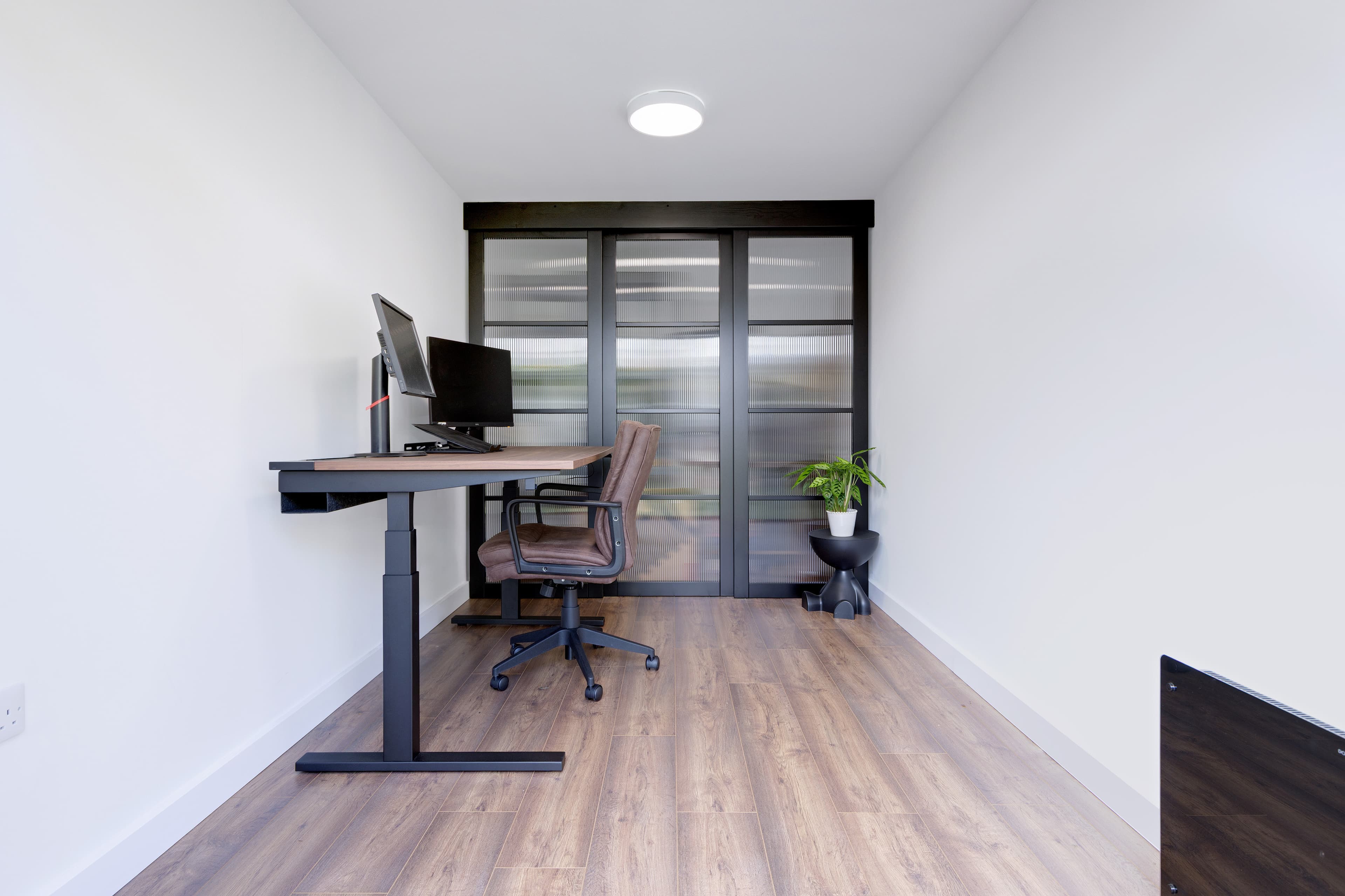 Garden office in Bedfordshire — quiet interior with reeded glass screen doors and a timber desk